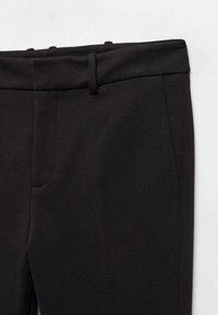 Pantalons noirs ajustés avec une texture lisse, dotés d'une taille avec passants de ceinture et de deux poches latérales. Le tissu semble durable et structuré.