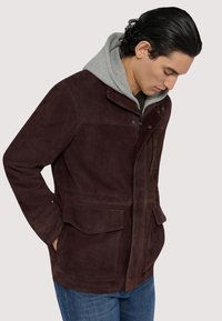 Brun mockakjol med en kordflätsad krage och dragkedja fram, med två framfickor och en lager av grå huvtröja under.