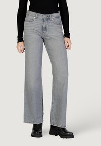 Jeans grigi ampi in denim, con chiusura a bottoni, tasche frontali e un lavaggio leggermente sbiadito. Indossati con stivali neri con plateau.