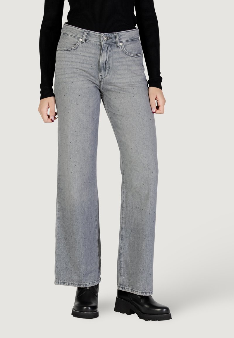 Jeans grigi ampi in denim, con chiusura a bottoni, tasche frontali e un lavaggio leggermente sbiadito. Indossati con stivali neri con plateau.