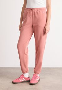 Zachte roze joggingbroek met een elastische tailleband en trekkoord. Gecombineerd met roze sneakers met witte strepen. Soepele textuur.