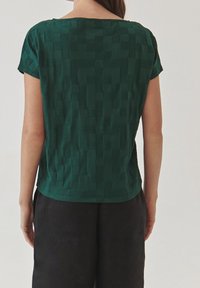 Top verde texturizado de manga corta con un patrón de cuadros, escote redondo y dobladillo recto, combinado con pantalones negros.