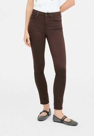 Femme portant un pantalon slim marron foncé associé à des chaussures plates à motifs noir et blanc avec double brides.