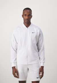 Weißer Sportjacke mit Reißverschluss vorne, hohem Kragen und schwarzem Nike-Logo. Hergestellt aus glattem, leichtem Stoff mit strukturierten Nähten.