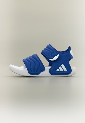 Sinine sandaal kahe laia, tekstuurse rihmaga, valge tallaga ja kolme valge triibuga logodetailiga välisküljel. Sobib vabaks kandmiseks.