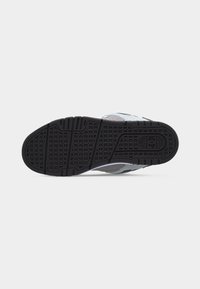 Σόλα ενός γκρι και άσπρου αθλητικού παπουτσιού με μαύρη ελαστική εξωτερική σόλα που διαθέτει τετράγωνα και γραμμικά σχέδια πέλματος και ένα μικρό λογότυπο κοντά στη φτέρνα.