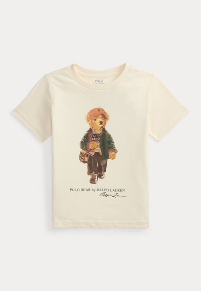 Κρεμ T-shirt με εικόνα αρκούδας που φοράει καπέλο, μπουφάν, πουλόβερ, παντελόνι και αθλητικά, κρατώντας μια τσάντα, με την επιγραφή Polo Bear από τη Ralph Lauren.