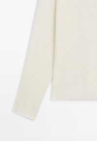 Cremfarbener Langarmpullover mit weichem, gestricktem Textur, vor einem weißen Hintergrund präsentiert.