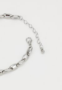 Collier en métal argenté avec des maillons allongés et un fermoir, présentant une chaîne de longueur ajustable avec un détail en perle ronde.