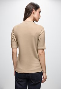 Beige kortærmet skjorte med rund halsudskæring, glat tekstur og afslappet pasform, parret med mørke denimjeans.