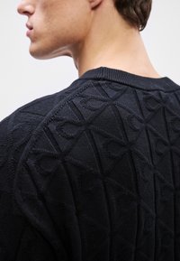 Maglione nero lavorato a maglia con un motivo geometrico testurizzato, scollo tondo e polsini a coste, che mette in risalto un design moderno e un materiale robusto.