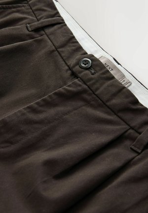 Tummanruskeat housut, jotka on valmistettu puuvillasekoitekankaasta. Niissä on napitus, sivutaskut ja etiketti, jossa on bränditiedot.