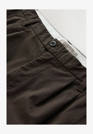 Tummanruskeat housut, jotka on valmistettu puuvillasekoitekankaasta. Niissä on napitus, sivutaskut ja etiketti, jossa on bränditiedot.