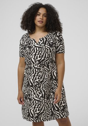 Woman with curly hair wearing a black and white animal print dress with short sleeves and a small front slit neckline.