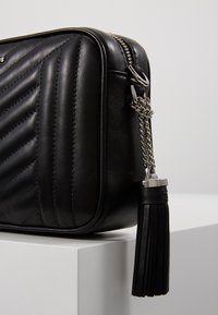 Schwarze Leder-Umhängetasche mit gequiltetem Muster, silbernem Zubehör und einer Quasten-Accente. Hat einen Reißverschluss und eine rechteckige Form.