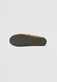 Suede slip-on shoe with a tan upper, stitched detailing, and a textured, dark grey rubber sole. Shape is flat and rounded at the toe.
