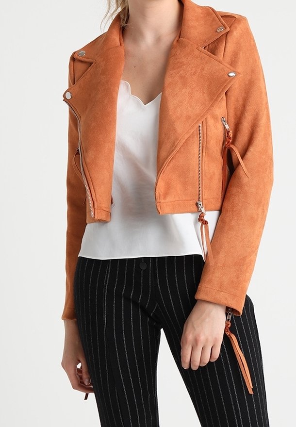 Ruosteenvärinen mokkanahkainen biker-takki, jossa vetoketjulliset taskut ja lyhyt malli. Yhdistetty valkoiseen yläosaan ja mustiin pinstripe-kuvioisiin housuihin.