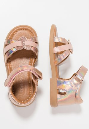 Sandalias rosas con acentos holográficos, tres correas cruzadas, hebilla ajustable y una suela marrón texturizada. Diseño plano para mayor comodidad.