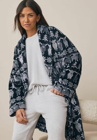 Marinblå kappa med vita djur- och snöflingemönster, tillverkad i mjukt tyg. Ljusgrå strukturerad outfit under med dragsko i midjan.