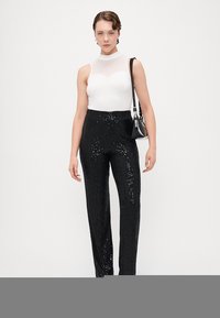 Biała bezrękawnik z wysokim dekoltem i czarnymi spodniami z cekinami, charakteryzującymi się dopasowanym krojem i prostymi nogawkami, dopełniony małą czarną torebką.