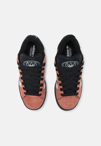 Nappasneakers i terrakotta och svart med svarta snören, utrustade med ett vitt diagonalt band och en märkesdetalj på tungan.