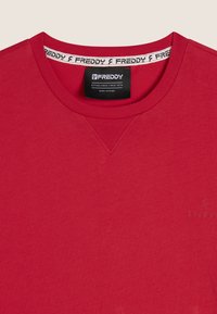 T-shirt rosso a maniche corte con scollo rotondo, caratterizzato da un logo sottile sul davanti e un'etichetta interna con marchio. Tessuto morbido.