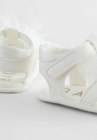 White fabric sandals featuring a tulle accent, open design, and adjustable straps. Smooth texture with stitching details visible.