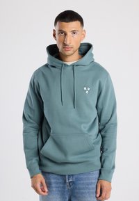 Groene hoodie van een zachte stof, met een kangoeroezak en een klein logo op de borst. De capuchon met trekkoord voegt detail toe.