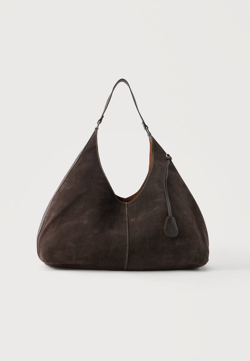 Sac hobo en daim marron foncé avec une seule bandoulière et une petite étiquette en cuir suspendue sur un fond clair uni.
