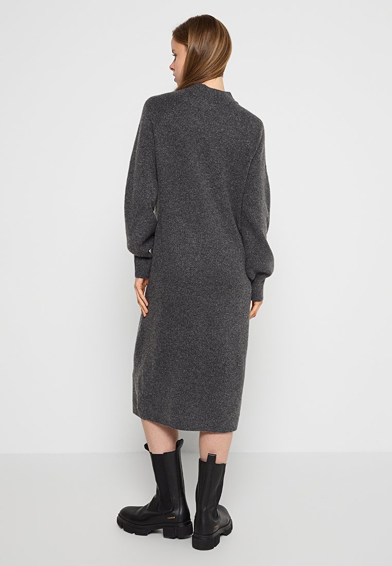 Langes, graues Strickkleid mit lockerer Passform, überschnittenen Schultern und gerippten Bündchen. Kombiniert mit kniehohen schwarzen Stiefeln. Strukturmaterial, bequem und kuschelig.