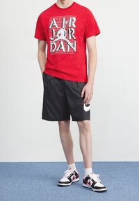 Červené bavlněné tričko s grafickým potiskem, černé šortky a černé a bílé tenisky s červenými akcenty. Jednoduchý design s atletickým střihem.