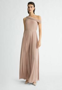 Een one-shoulder jumpsuit in zachte blush met een getailleerde bovendel, elastische tailleband en vloeiende wijde pijpen.