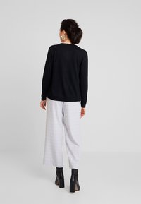 Sort sweater med lange ærmer, kombineret med lysegrå ternede bukser med vide ben. Sorte ankelstøvler fuldender outfittet.