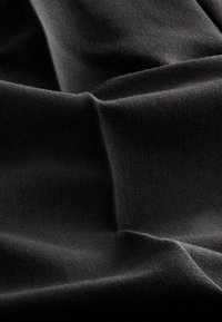 Tissu noir avec une texture lisse, présentant des plis subtils et une finition mate. Le matériau semble dense avec un motif tissé.