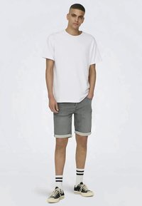 T-shirt branca de manga curta, calções de ganga cinza com bainhas enroladas, meias listradas em preto e branco e ténis pretos. Conjunto casual simples.