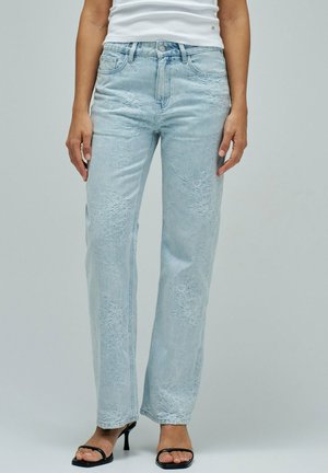 Vaqueros azul claro de pierna recta con bordado floral sutil, combinados con sandalias de tacón negras y una camiseta blanca sin mangas.