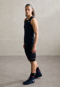 Čierny športový tielko s logom, doplnené čiernymi šortkami strednej dĺžky s sieťovanými doplnkami a modrými vysokými teniskami s červenými detailami.