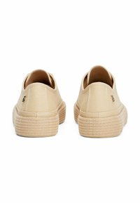 Baskets en toile beige avec une semelle en caoutchouc texturé, présentant un design minimaliste et un détail de marque subtil au niveau du talon.