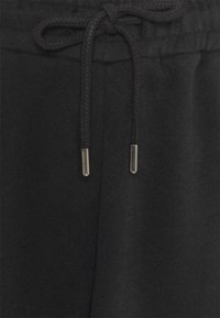 Black sweatpants feature a braided drawstring with metal tips and a soft, textured fabric. The waistband is elastic for comfort.