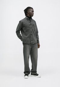 Camisa de ganga cinza com botões, jeans cinzentos soltos e sapatilhas pretas. Textura suave, design casual, com um bolso lateral na camisa.