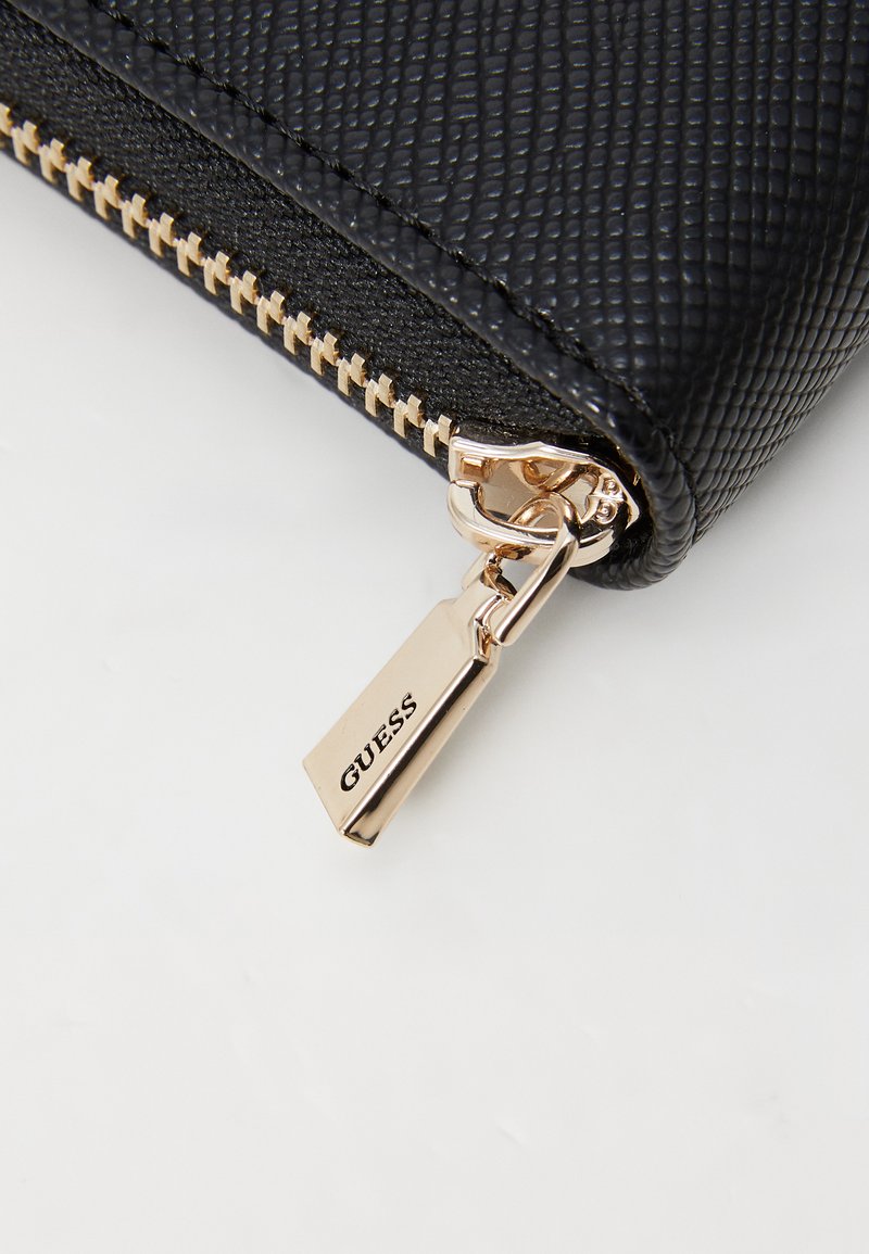 Portafoglio nero texture con zip dorata e un charm con il marchio. Presenta una forma rettangolare elegante e un'eccellente fattura.