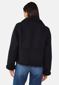 Giacca nera cropped con collo e polsini testurizzati e morbidi, caratterizzata da un design con cuciture visibili e una finitura in tessuto liscia.