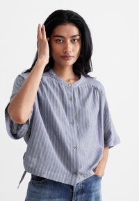 Gestreept, kortemouwenshirt in blauw en wit met groene accenten, knoopsluiting aan de voorkant, ronde halslijn en een losse pasvorm, gecombineerd met denimjeans.