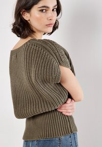 Oliwkowy sweter z dzianiny o teksturowanym, prążkowanym wzorze. Posiada krótkie rękawy i dopasowany dół. Noszony z dżinsami.