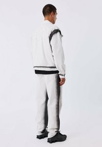 Chaqueta de mezclilla gris claro y pantalones a juego con acentos en degradado negro. Presenta un corte relajado y detalles de costura visibles. Zapatillas negras.