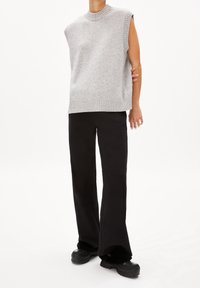 Lekka szara bezrękawnikowa kamizelka z prążkowanym dekoltem i dołem, zestawiona z czarnymi rozszerzanymi spodniami i masywnymi czarnymi butami. Gładka faktura na całej powierzchni.