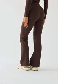 Brązowe legginsy rozszerzane wykonane z elastycznej tkaniny, z wysokim stanem i gładką fakturą, zestawione z jasnymi sneakersami.