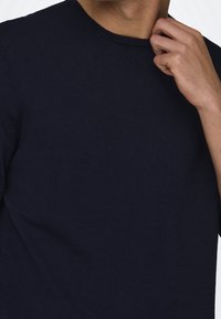 T-shirt en maille bleu marine avec un col rond et des manches courtes, présentant une texture lisse et une coupe ajustée. Aucun motif ou accent notable.