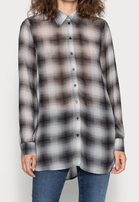 Langärmliges, knopfbares Hemd aus transparenter Stoff mit einem schwarzh, weißen und grauen Karomuster. Verfügt über einen klassischen Kragen und einen abgerundeten Saum.