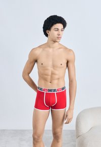 Sarkanas bokseršorti no elastīga auduma ar melnu jostasvietu, kurā baltā krāsā rakstīts zīmola nosaukums "DIESEL".